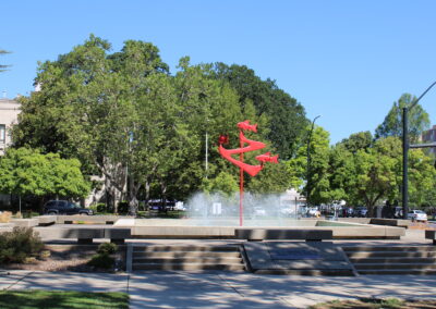 A photo of a water fountain with a red art piece in the middle.