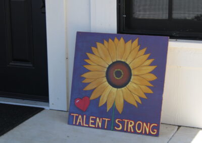 A painting of a sunflower and a heart that reads "Talent Strong"
