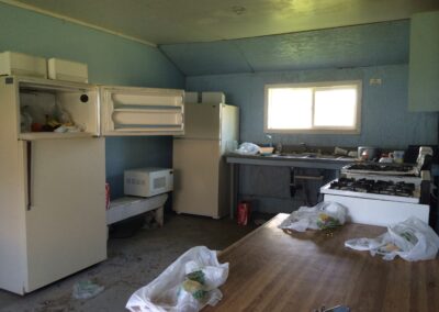 A photo of a kitchen with two fridges, two stoves, and garbage.